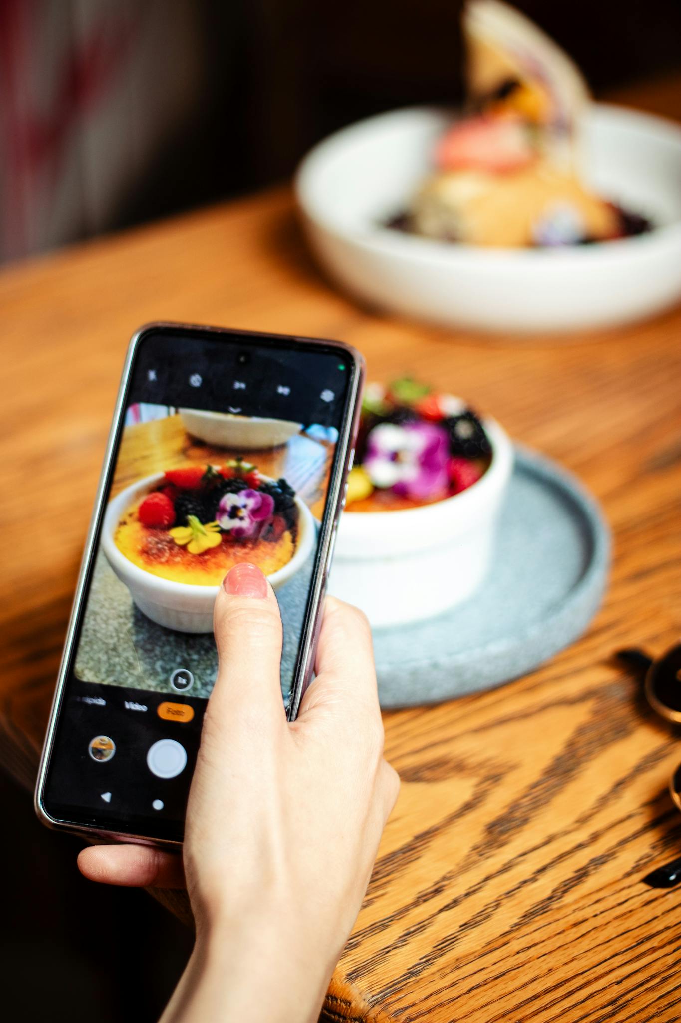 A vibrant dessert being captured on a smartphone, showcasing food photography in a cafe setting.