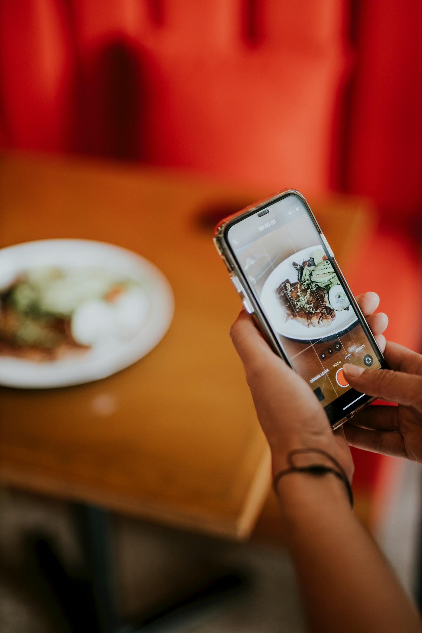 A woman photographs a gourmet meal in a restaurant with her phone.