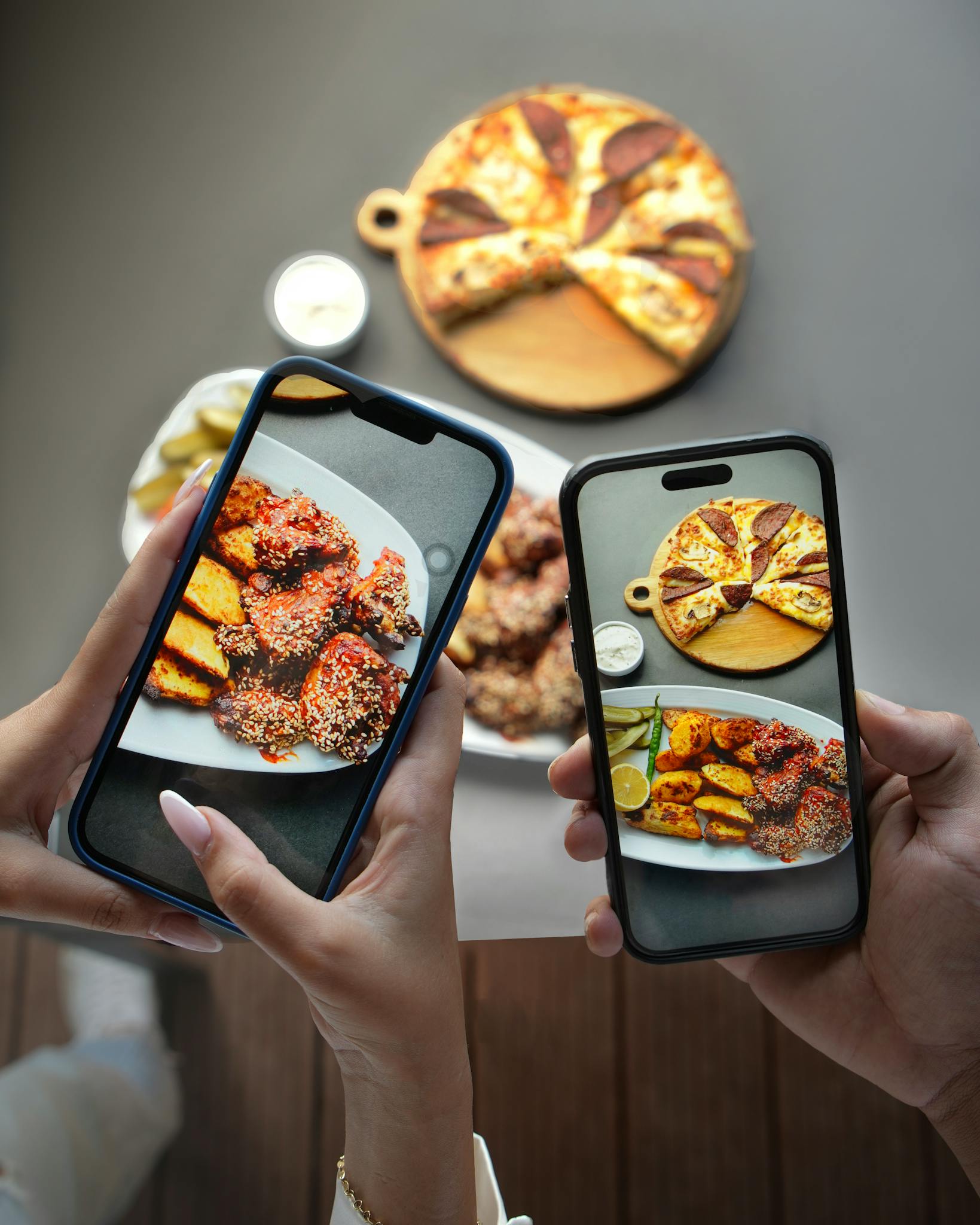Close-up of hands photographing chicken and pizza with smartphones in a cafe.