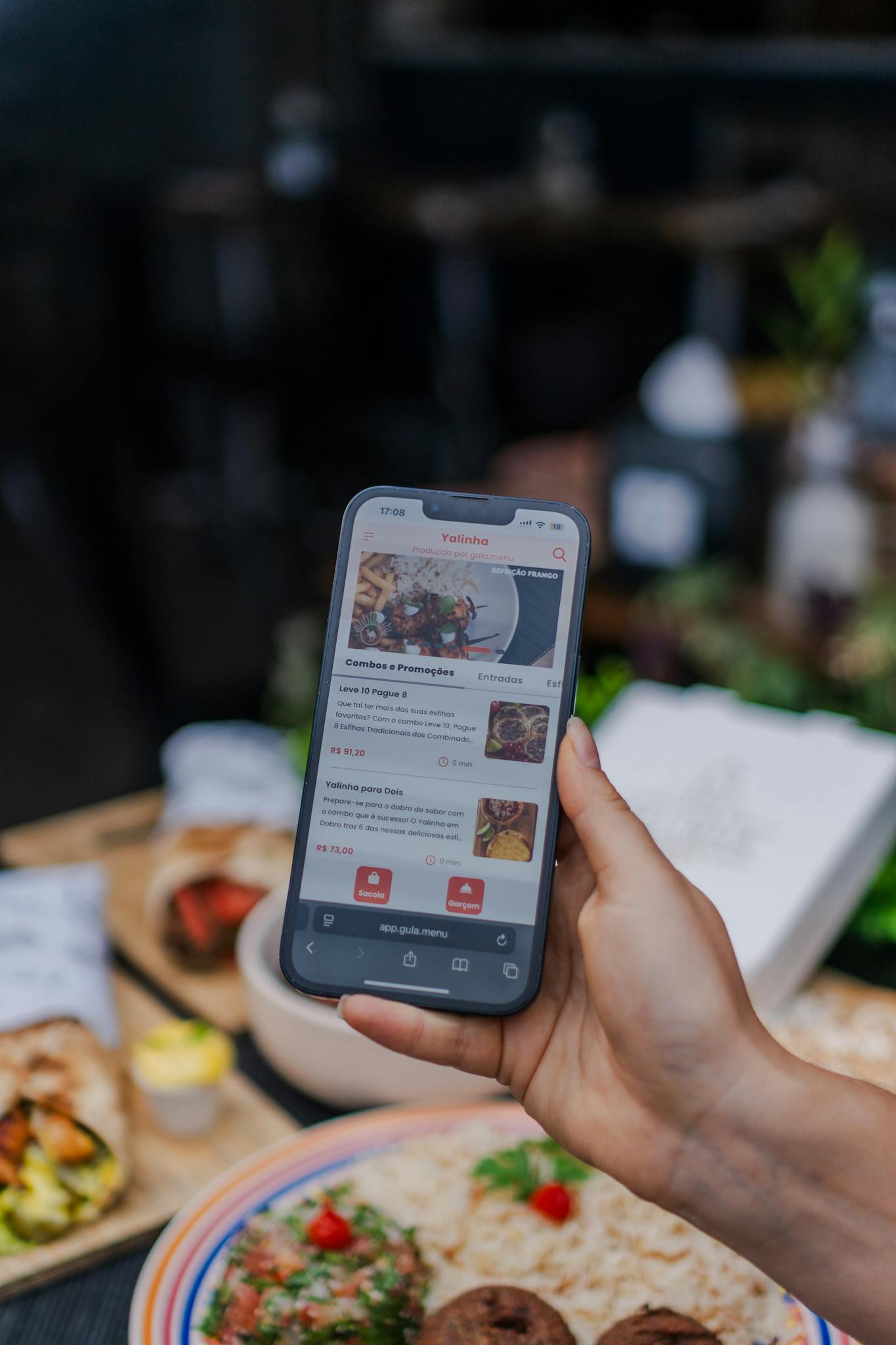Hand holding a smartphone displaying a food delivery app screen in a restaurant setting.